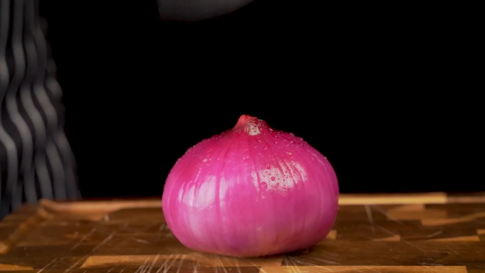 A red onion on the board, whole. Half the argument for a sharp knife is what does not happen to your eyes.